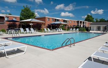 A swimming pool surrounded by sun loungers and apartment buildings.